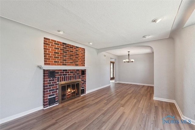 3105 W Laskey Rd, Toledo, OH 43613 - unfurnished living room featuring wood finished floors, arched walkways, baseboards, a chandelier, and a textured ceiling