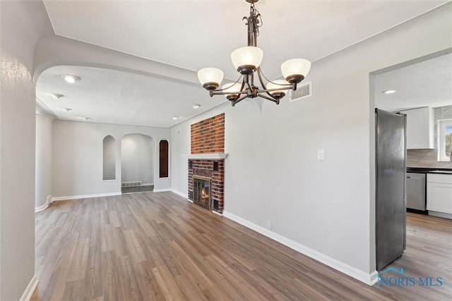 3105 W Laskey Rd, Toledo, OH 43613 - unfurnished living room with arched walkways, visible vents, a chandelier, light wood-style floors, and a brick fireplace