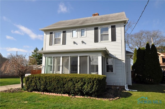 traditional home featuring a chimney, a sunroom, and a front lawn