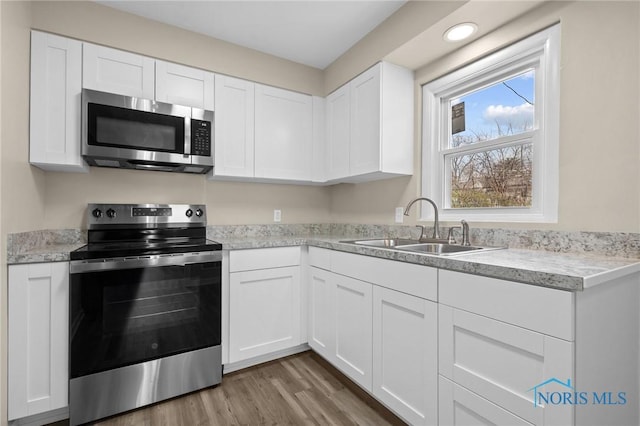 kitchen featuring stainless steel appliances, a sink, white cabinetry, wood finished floors, and light countertops