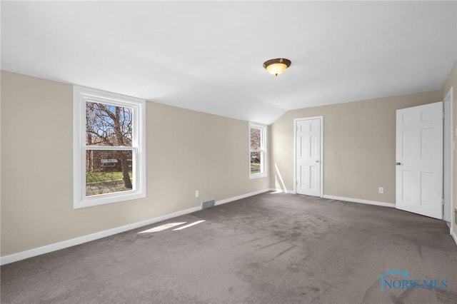 spare room featuring dark carpet, baseboards, visible vents, and plenty of natural light