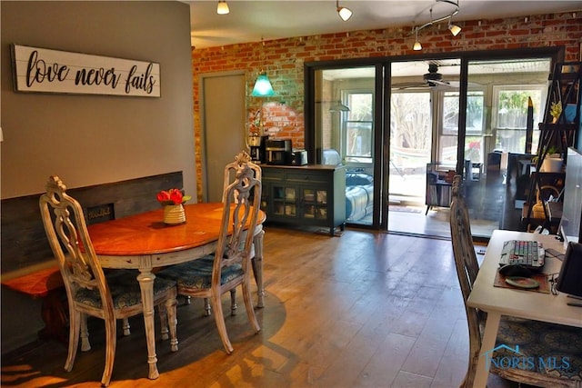 dining area with wood-type flooring and brick wall