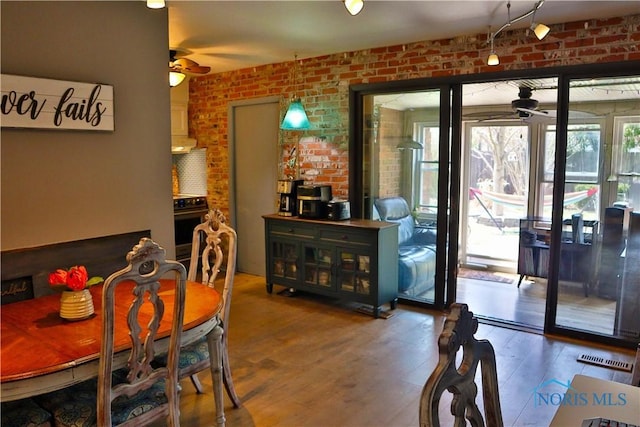 dining area featuring wood finished floors, visible vents, a ceiling fan, and brick wall