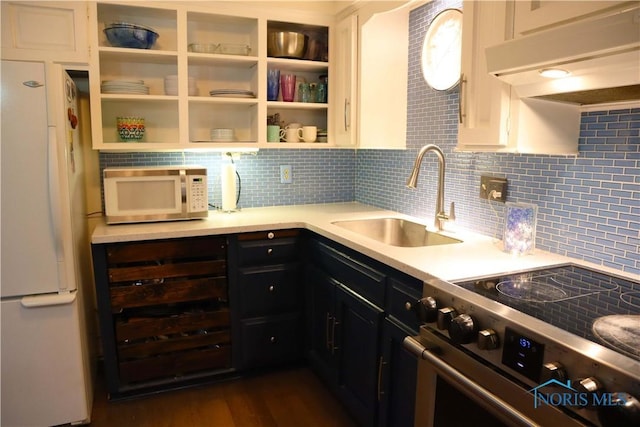 kitchen featuring under cabinet range hood, light countertops, a sink, white appliances, and decorative backsplash