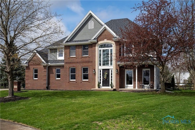 view of front of home with brick siding, a shingled roof, a front lawn, and fence