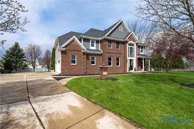view of front of property featuring brick siding, concrete driveway, a front lawn, and fence