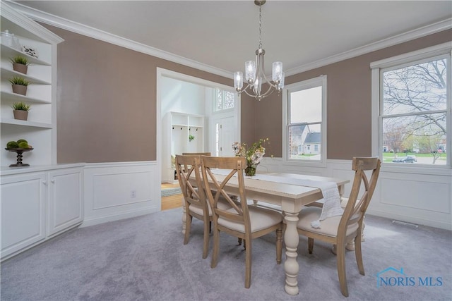 dining space featuring a notable chandelier, light carpet, ornamental molding, and wainscoting