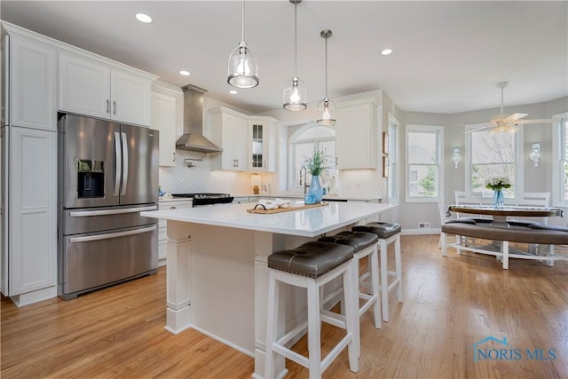 kitchen featuring wall chimney exhaust hood, white cabinets, backsplash, light countertops, and appliances with stainless steel finishes
