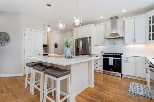 kitchen with wall chimney range hood, electric range oven, light wood-style flooring, stainless steel refrigerator with ice dispenser, and white cabinetry