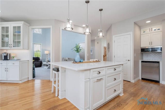 kitchen with stainless steel appliances, light wood-type flooring, pendant lighting, glass insert cabinets, and white cabinetry