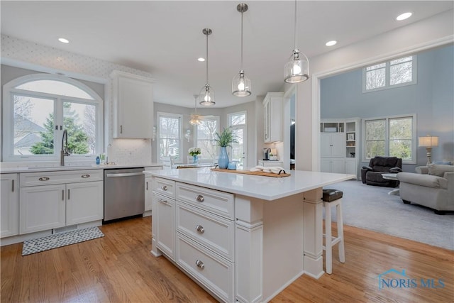 kitchen with a breakfast bar, light countertops, dishwasher, a sink, and white cabinetry