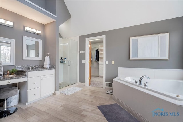 full bath featuring a bath, a spacious closet, wood finished floors, a shower stall, and vanity