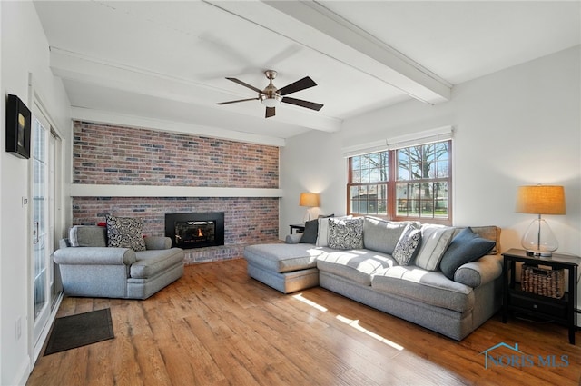 living area with beamed ceiling, wood finished floors, a fireplace, and a ceiling fan