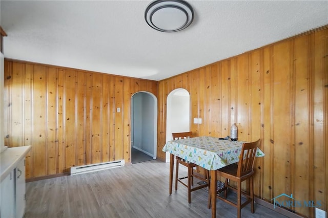 402 S 5th St, Continental, OH 45831 - dining room featuring a baseboard heating unit, arched walkways, wood walls, and wood finished floors