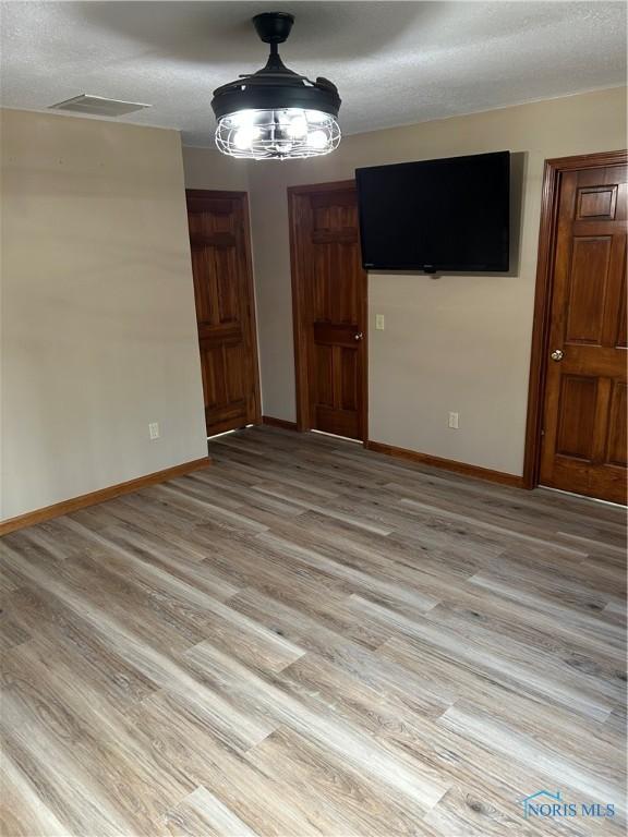 unfurnished dining area with light wood-style floors, a textured ceiling, baseboards, and visible vents