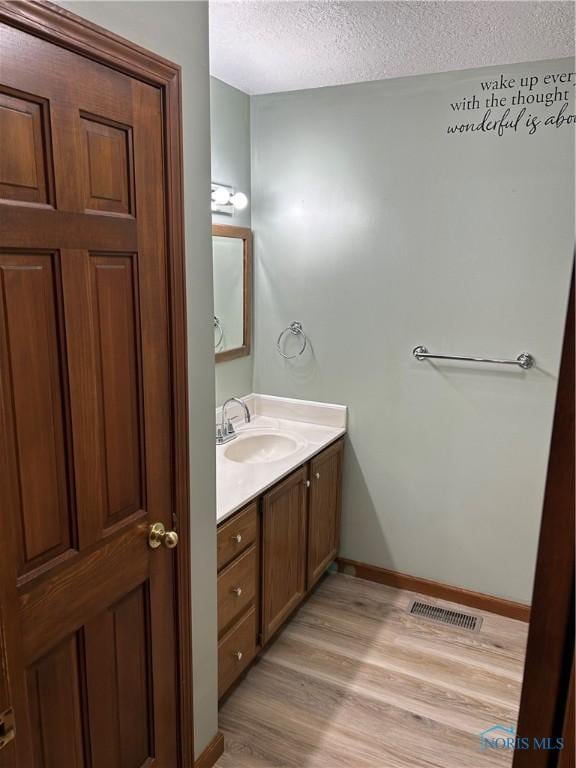 bathroom featuring wood finished floors, a textured ceiling, vanity, baseboards, and visible vents