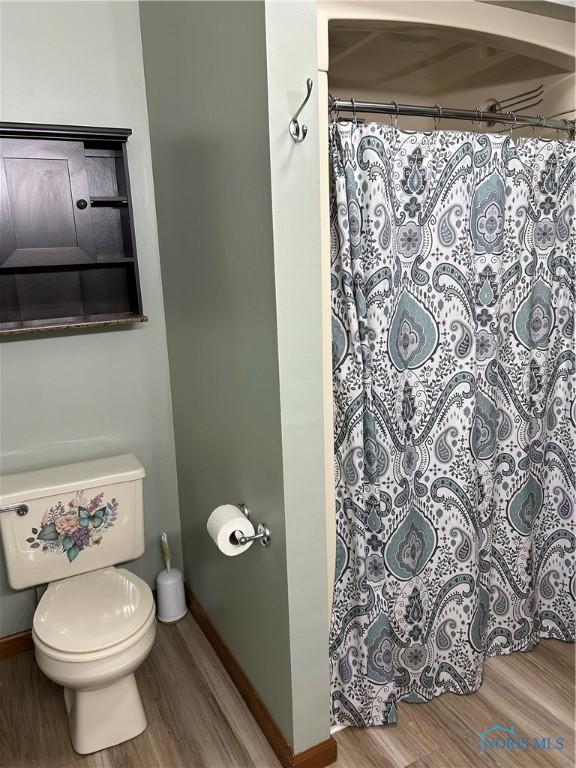 full bathroom featuring baseboards, wood finished floors, curtained shower, and toilet