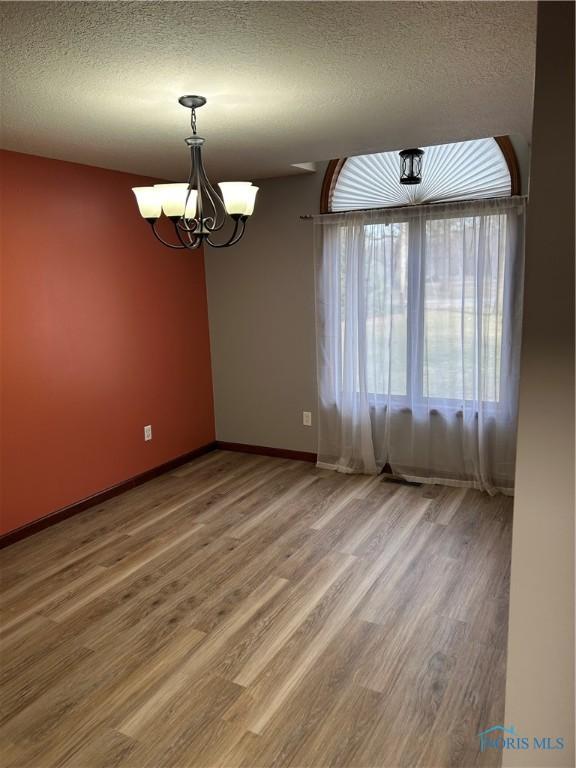 unfurnished room featuring baseboards, wood finished floors, a chandelier, and a textured ceiling
