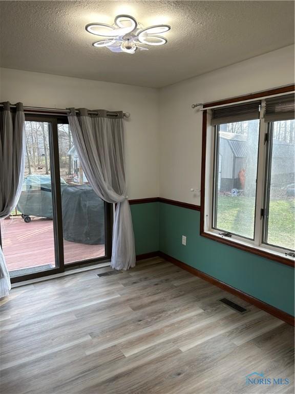 spare room featuring baseboards, a textured ceiling, visible vents, and light wood-style flooring