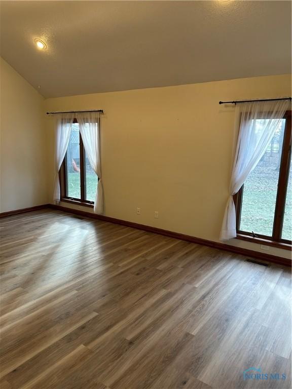 unfurnished room with vaulted ceiling, baseboards, wood finished floors, and visible vents