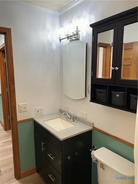 half bath featuring wood finished floors, toilet, vanity, and ornamental molding