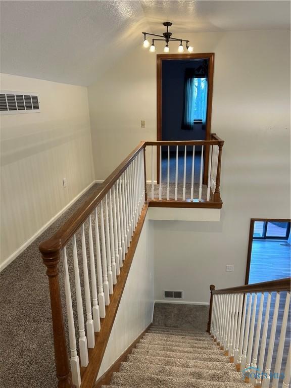 staircase with baseboards, vaulted ceiling, visible vents, and carpet flooring