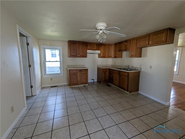 kitchen featuring a sink, a ceiling fan, brown cabinets, and baseboards