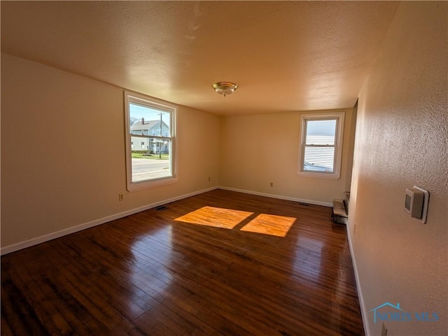empty room featuring visible vents, hardwood / wood-style floors, a textured ceiling, and baseboards