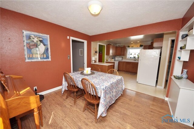 dining space with baseboards, a textured ceiling, and light wood finished floors