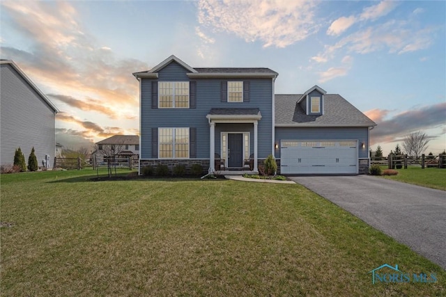 traditional home featuring driveway, stone siding, a front yard, and fence
