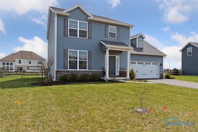 view of front of house featuring driveway, stone siding, fence, a shingled roof, and a front yard