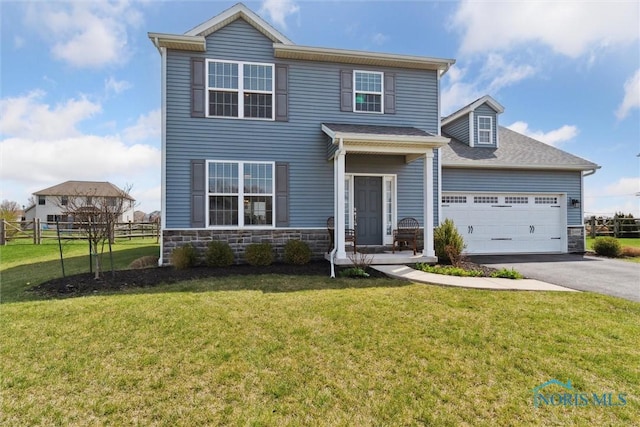 traditional home with a front lawn, driveway, stone siding, fence, and a garage