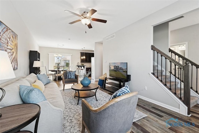 living area featuring stairs, wood finished floors, ceiling fan with notable chandelier, baseboards, and visible vents