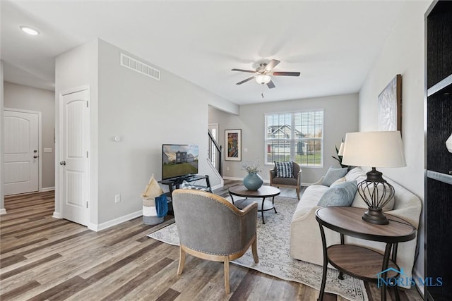 living area featuring wood finished floors, visible vents, baseboards, and ceiling fan