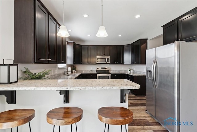 kitchen featuring stainless steel appliances, a peninsula, recessed lighting, wood finished floors, and hanging light fixtures