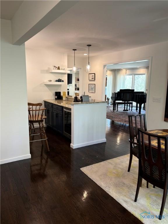 kitchen featuring hanging light fixtures, light stone counters, baseboards, a peninsula, and dark wood-type flooring
