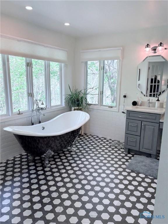 bathroom with tile walls, a freestanding tub, a wainscoted wall, and vanity