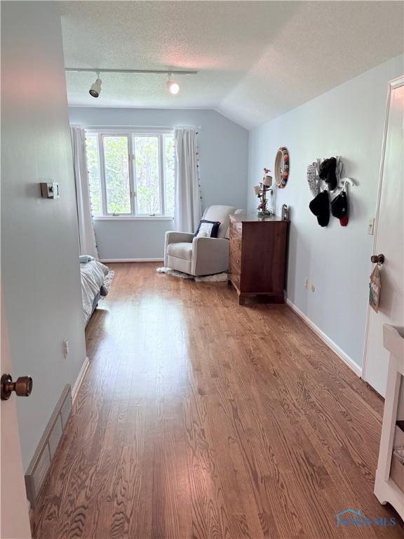 bedroom with rail lighting, wood finished floors, visible vents, and baseboards