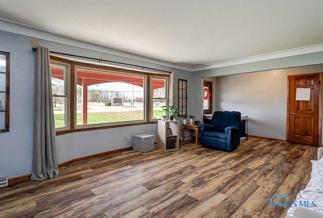 living area with visible vents, baseboards, wood finished floors, and ornamental molding