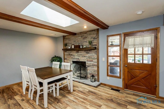 dining room with baseboards, light wood-style floors, beamed ceiling, a skylight, and a fireplace