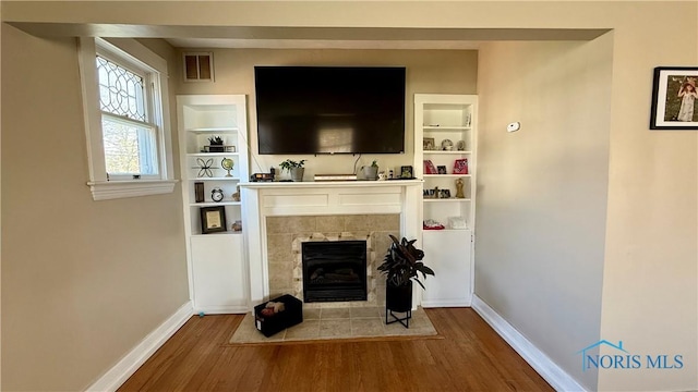 living area with baseboards, wood finished floors, visible vents, and a tile fireplace