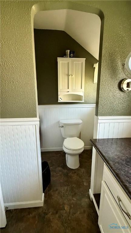 bathroom featuring wainscoting, toilet, a textured wall, and vanity