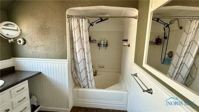 full bath featuring shower / tub combo with curtain, vanity, a textured wall, and wainscoting