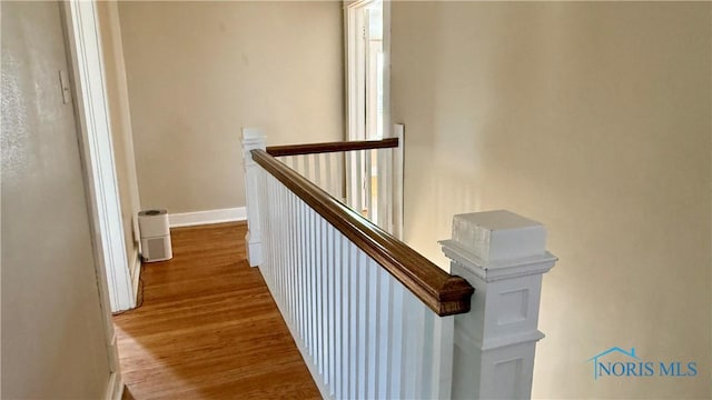 corridor with wood finished floors, baseboards, and an upstairs landing