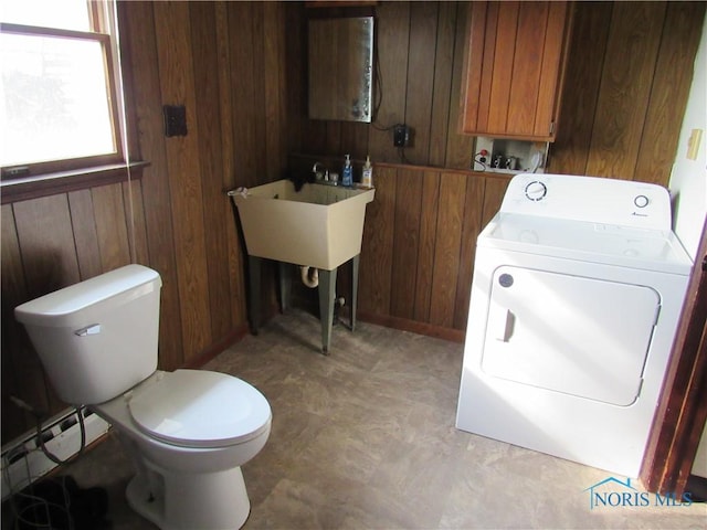 bathroom with a baseboard radiator, wood walls, toilet, and washer / clothes dryer