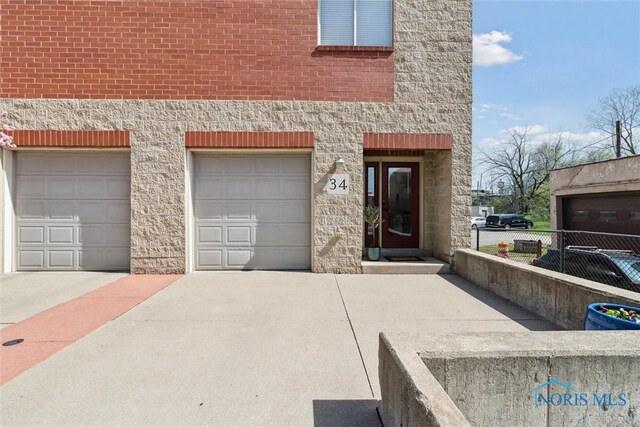 view of front of property featuring concrete driveway, fence, and stone siding