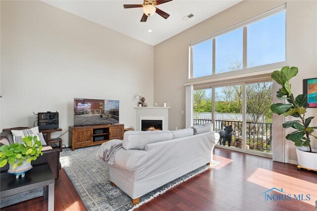 living room featuring visible vents, wood finished floors, ceiling fan, a high ceiling, and a lit fireplace