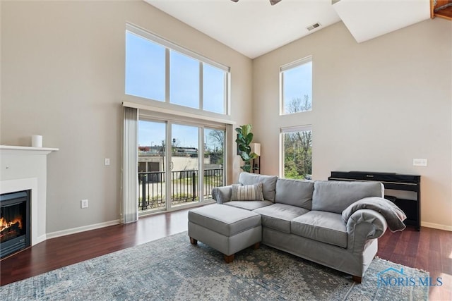 living area featuring a glass covered fireplace, a towering ceiling, wood finished floors, and visible vents