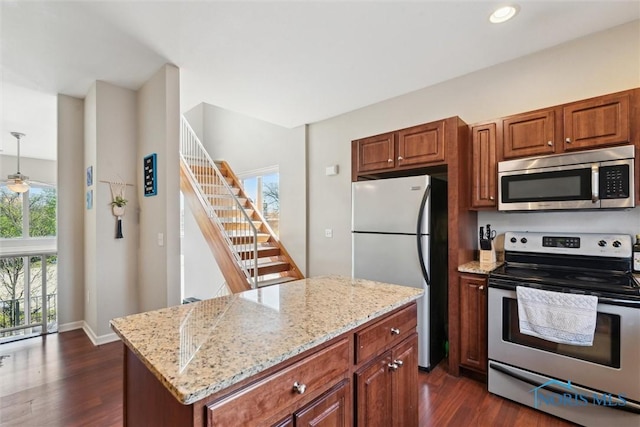 kitchen with appliances with stainless steel finishes, a center island, dark wood-style flooring, and light stone counters