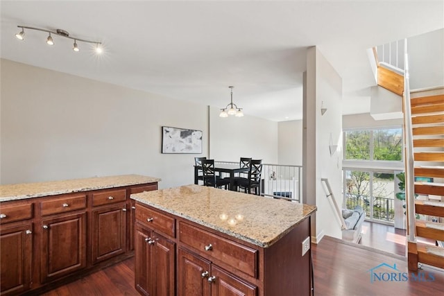 kitchen featuring a kitchen island, light stone counters, dark wood finished floors, a notable chandelier, and decorative light fixtures